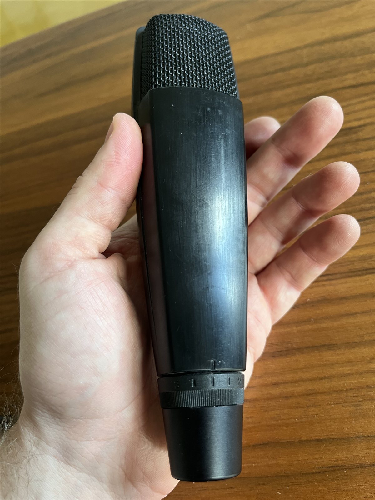 A compact studio microphone held in a hand.